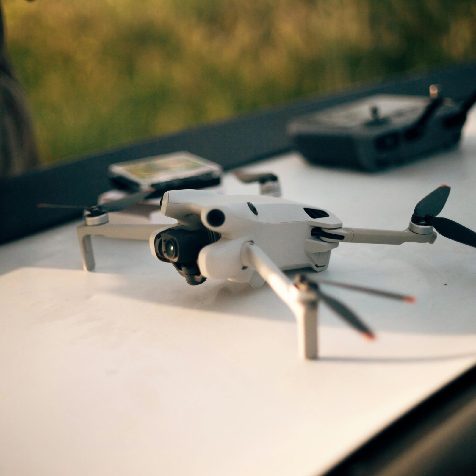 Small white drone and remote controller on a white surface outdoors.